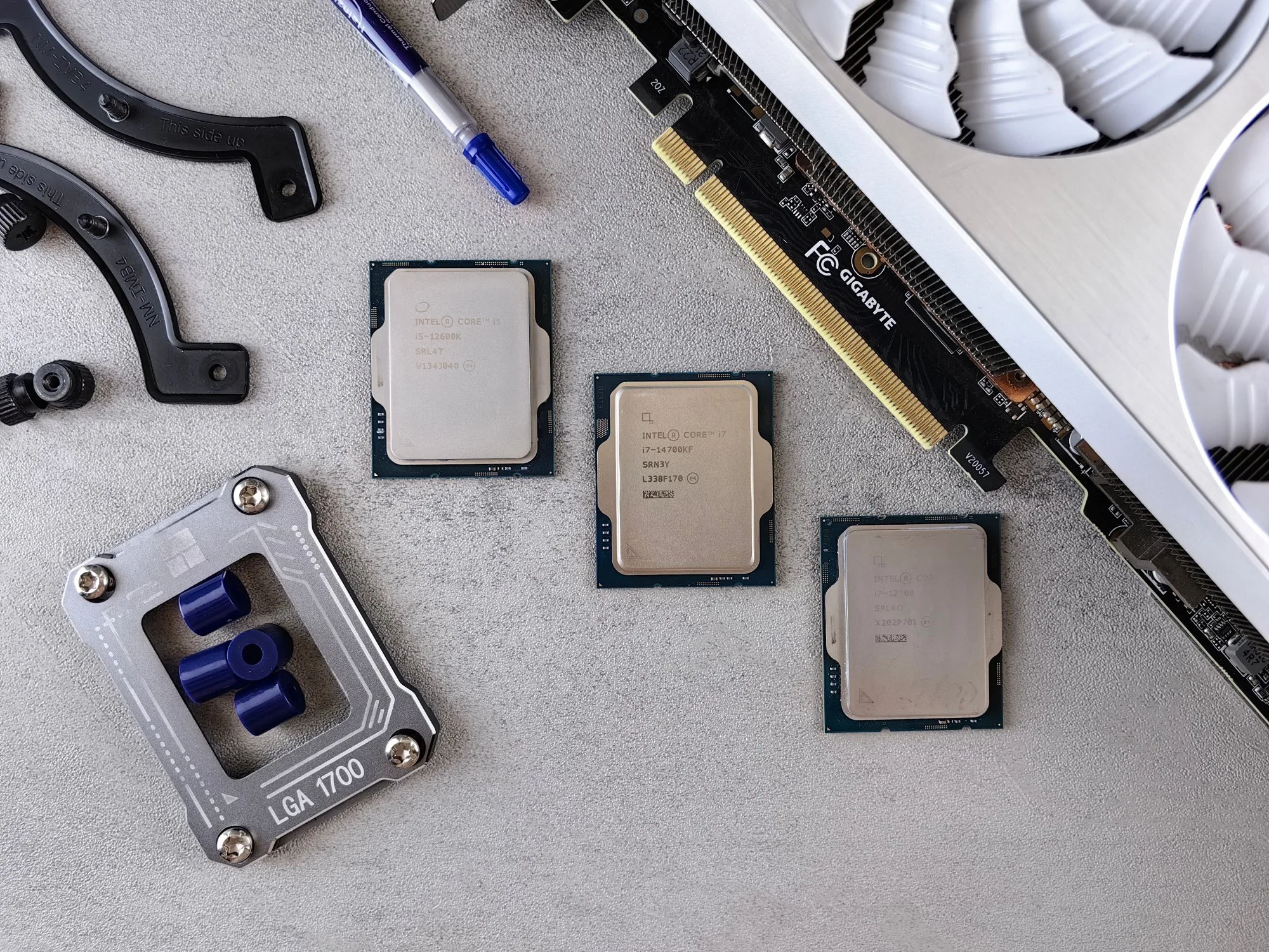 Desktop processors, a graphics card and CPU mounting parts laid out on a grey surface